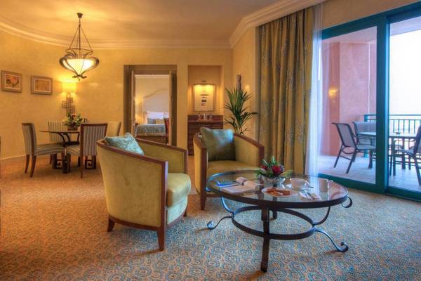 Wohnbereich der Atlantis The Palm Suite mit zwei Sesseln, Tisch, Blumen und offenem Balkon.
