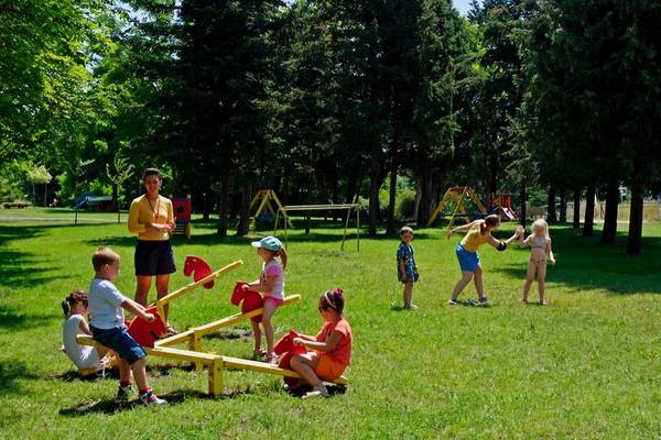 Kinder spielen im Park mit Rutschbahnen und Schaukeln unter Aufsicht von Erwachsenen.