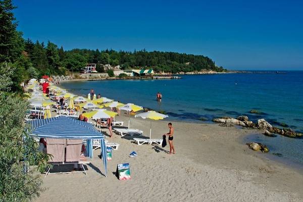 Ein sonniger Strand mit vielen Sonnenschirmen und Personen, einige schwimmen im Wasser.