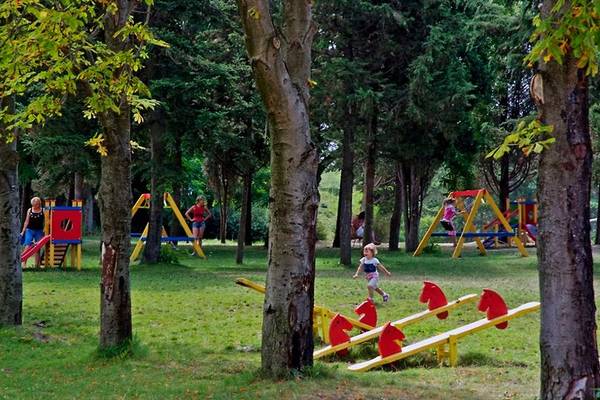 Kinderspielplatz im Freien im Sol Nessebar Palace Hotel mit Bäumen und Spielgeräten.