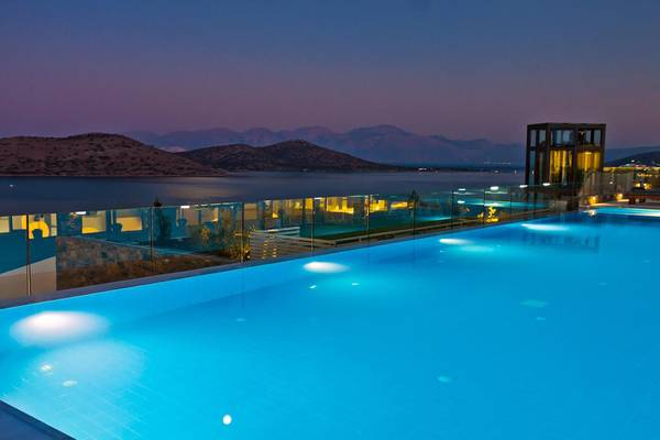 Ein Swimmingpool des Royal Marmin Bay Hotels bei Nacht mit blauem Wasser und Bergpanorama.