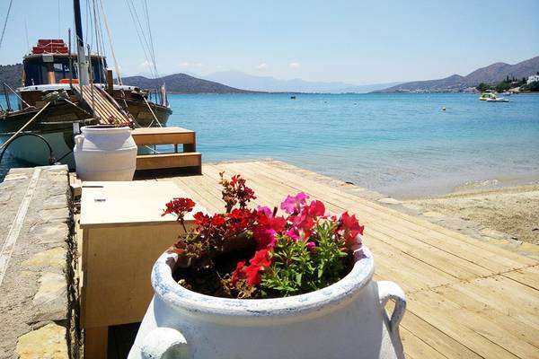 Strand mit Boot im Wasser und Blumentopf mit roten und pinken Blumen.