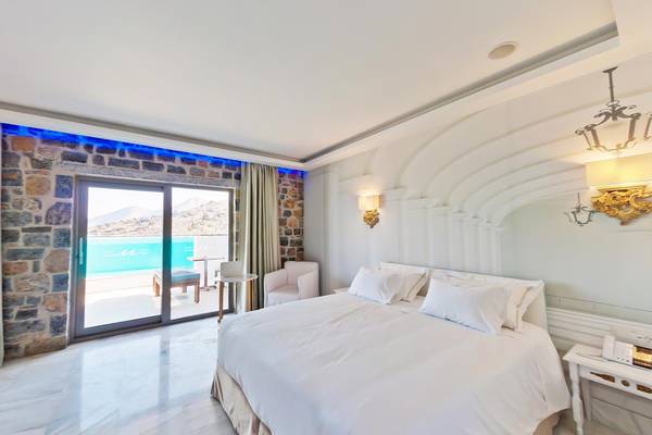 Schlafzimmer im Royal Marmin Bay Boutique Hotel mit großem Bett, weißem Kopfteil und Ausblick auf den Pool.