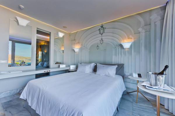 Schlafzimmer im Royal Marmin Bay Boutique Hotel mit Doppelbett, weißer Bettwäsche, Tisch mit Champagner und Glas sowie eleganter Wandgestaltung.