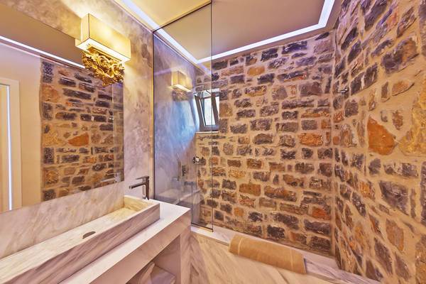 Badezimmer im Royal Marmin Bay Boutique Hotel mit Natursteinwand und Glasdusche.