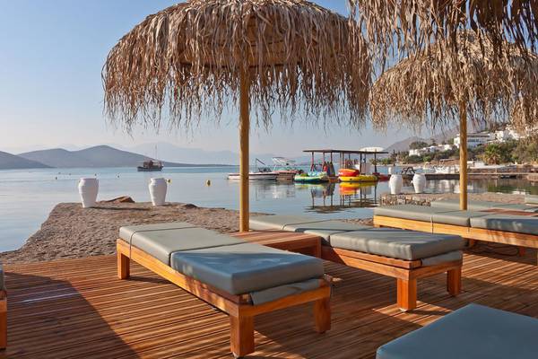 Lounge-Bereich des Royal Marmin Bay Boutique Hotels mit Holzliegen und Strohschirmen am Strand.