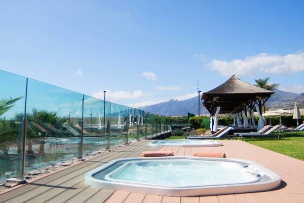 Außenbereich des Gran Melia Palacio de Isora Hotels mit zwei Whirlpools, einem Pool und Sonnenliegen.