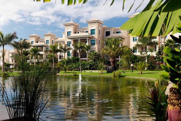 Gran Melia Palacio de Isora Hotel mit Teich und Palmen im Vordergrund.