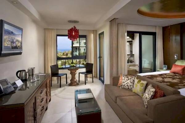 Innenansicht einer Suite im Gran Melia Palacio de Isora Hotel mit Bett, Couch, Tisch und Fernseher.