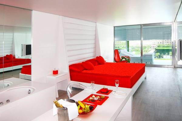 Schlafzimmer im Adam & Eve Hotel mit roten Möbeln, Bett, Tisch mit Früchten und Champagner, und Ausblick.