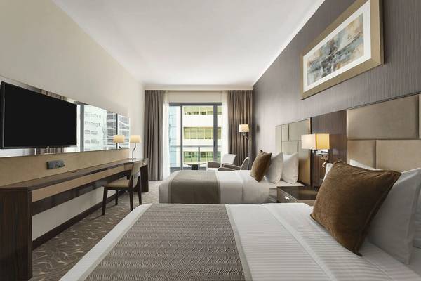 Zimmer im Hawthorn Suites Abu Dhabi mit zwei Betten, Fernseher, Schreibtisch und Fenster mit Stadtblick.