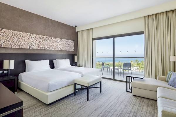 Hotelzimmer mit zwei Betten, Meerblick und großem Fenster.
