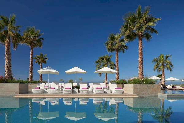 Pool-Loungebereich im Hyatt Place Taghazout Bay Hotel mit weißen Sonnenliegen und Schirmen.