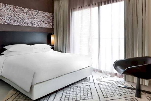 Ein modernes Bettzimmer im Hyatt Place Taghazout Bay mit weißen Laken, zwei Nachttischen und einer gemusterten Wand.