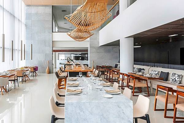 Innenansicht des Restaurants im Hyatt Place Taghazout Bay mit mehreren Tischen, Stühlen und Dekorationen.