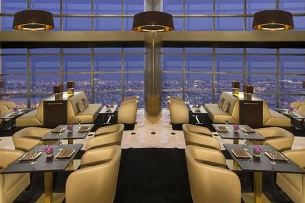 Innenbereich des Jumeirah Emirates Towers Hotels mit goldenen Stühlen und Tischen, großen Fenstern mit Blick auf die Stadt.