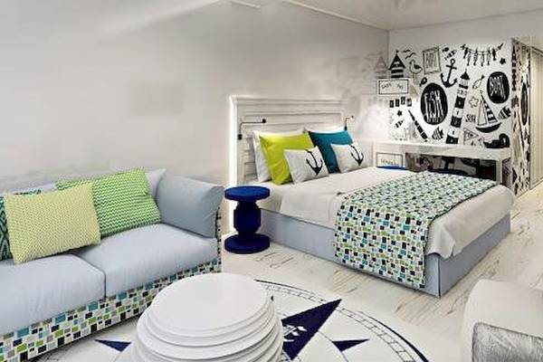 Inneneinrichtung des Zimmers im Amadria Park Beach Hotel Jure mit weißen Wänden, einem Bett, einem Sofa, bunten Kissen und maritimen Wanddekorationen.