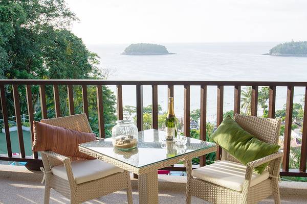 Balkon mit Meerblick im Andaman Cannacia Resort mit Tisch, Flasche und Gläsern.