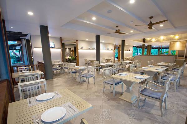 Innenansicht des Restaurants im Andaman Cannacia Resort mit leeren Tischen und Stühlen, Deckenventilatoren und einer Theke.