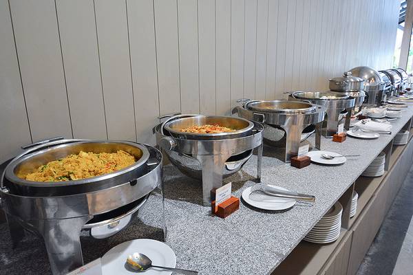Buffet-Tisch im Andaman Cannacia Resort mit verschiedenen Gerichten in Silberschüsseln und leeren Tellern.
