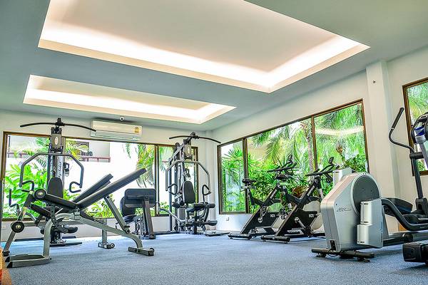 Fitnesscenter im Andaman Cannacia Resort mit verschiedenen Geräten und großen Fenstern.