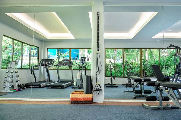 Fitnesscenter im Andaman Cannacia Resort mit Spiegeln, Laufbändern und Fenstern.
