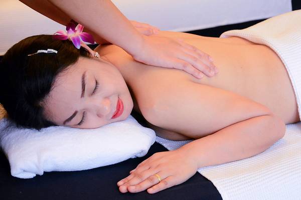 Frau im Andaman Cannacia Resort genießt eine Massage mit einem weißen Handtuch und einer Blume im Haar.
