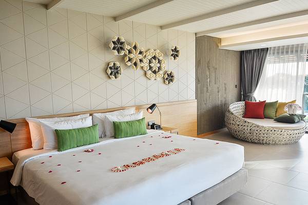 Zimmer im Andaman Cannacia Resort mit einem großen Bett und einem Sofa, beide mit vielen Kissen und einer Tisch mit Lampen.