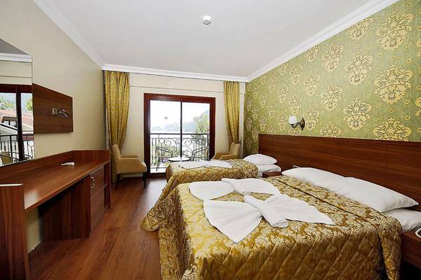 Zwei Betten in einem Hotelzimmer des Meril Hotels, beide mit Bettdecken und Kissen, vor einem Balkon mit Fenster.