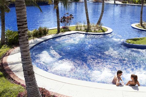 Ein Swimmingpool mit zwei Personen, die im Wasser sitzen, im Barcelo Maya Palace.