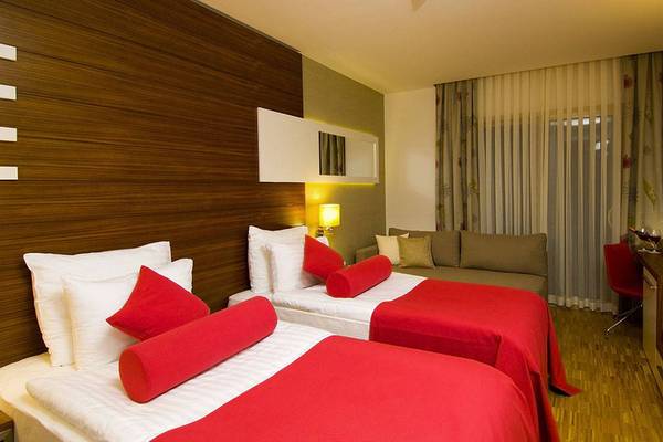 Doppelzimmer im Blue Waters Club Hotel mit zwei Betten, roten Decken und Kissen, einem Sofa und einer Fernseher.