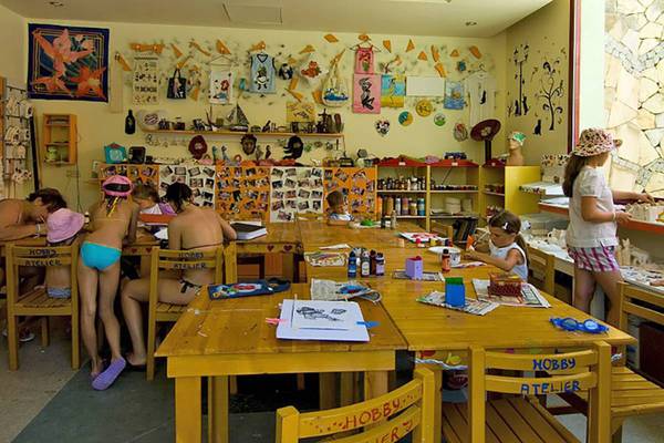 Im Blue Waters Club nehmen Kinder an einem Malkurs teil, während eine Frau im Hintergrund Bilder malt.