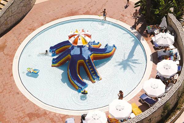 Luftaufnahme des Pools im Blue Waters Club mit einer großen Wasserrutsche und Gästen, die um den Pool herum entspannen.