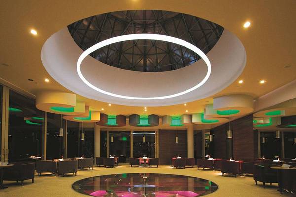 Lobby des Blue Waters Club Hotels mit zentraler Lichtinstallation und gerundeten Möbeln.