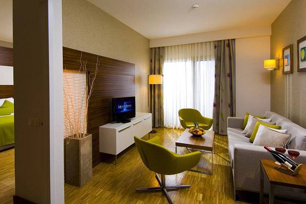 Innenansicht eines Zimmers im Blue Waters Club Hotel mit Bett, Fernseher, Couch, Stühle und Tisch.