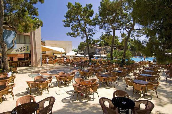 Im Freien gelegenes Restaurant des Blue Waters Club mit vielen Tischen und Stühlen, umgeben von Bäumen und einer Wasserlandschaft.