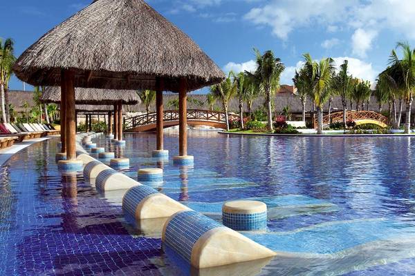 Außenpool des Barcelo Maya Palace mit tropischen Palmen und einer Brücke im Hintergrund.