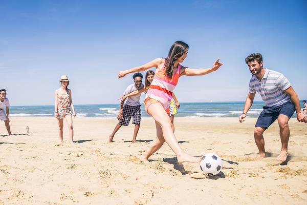 Gruppe von Menschen, die Fußball auf dem Strand spielen, bei klarem Himmel.