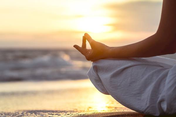 Person in Yoga Meditation am Strand bei Sonnenuntergang