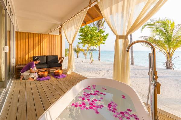 Außenbadewanne am Innahura Maldives Resort mit Blick auf den Ozean und Palmen.