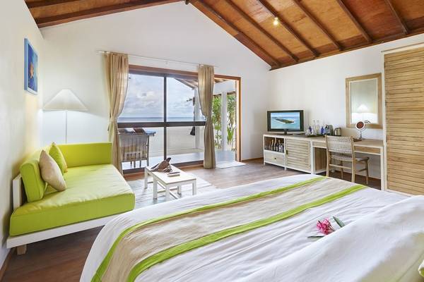 Innenansicht des Schlafzimmers im Innahura Maldives Resort mit grüner Couch, Fernseher, Schreibtisch und Meerblick.