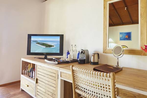 Innenansicht eines Zimmers im Innahura Maldives Resort mit Fernseher, Schreibtisch, Spiegel und Blumenvase.