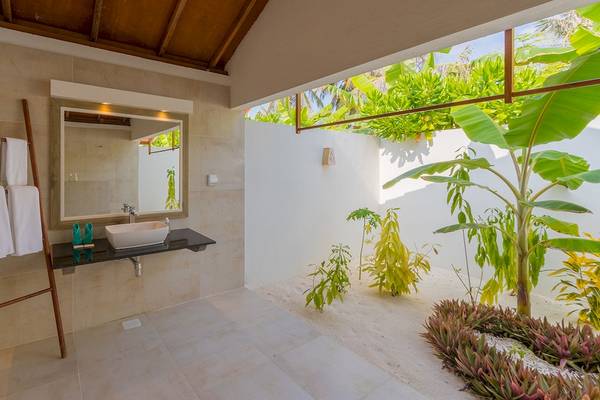 Innenansicht eines Badezimmers im Innahura Maldives Resort mit einem Waschbecken, Spiegel und Pflanzen.