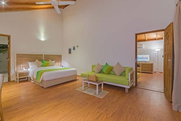 Innenansicht eines Hotelzimmers im Innahura Maldives Resort mit grüner Couch, Bett und Holzboden.