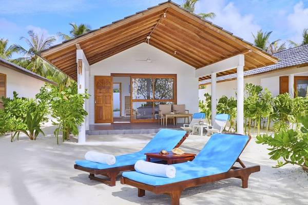 Außenbereich der Innahura Maldives Resort Villa mit zwei blauen Liegen und einem Tisch auf einem sandigen Strand.