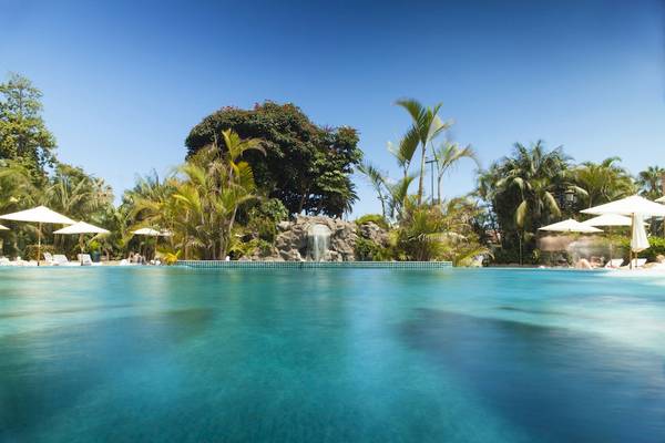 Ein großer Swimmingpool im Botanico & The Oriental Spa Garden Hotel, umgeben von Bäumen und Sonnenschirmen.