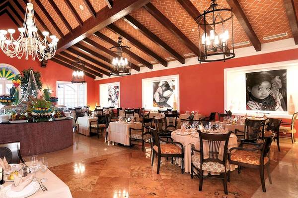 Innenbereich des Restaurants im Barcelo Maya Palace Hotel mit roten Wänden, Tischdecken und Kronleuchtern.