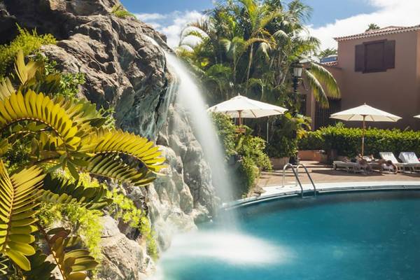 Außenpool des Botanico & The Oriental Spa Garden Hotels mit Wasserfall und Sonnenschirmen.