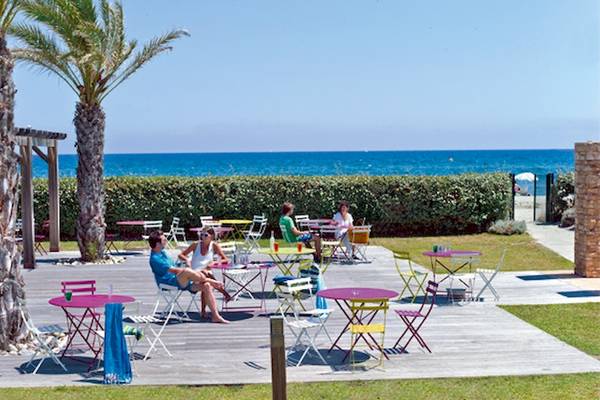Gäste sitzen an farbenfrohen Tischchen auf der Terrasse von Belambra Clubs Pineto am Strand.