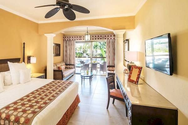 Hotelzimmer im Barcelo Maya Palace mit Bett, Wohnzimmer und Terrassentür.